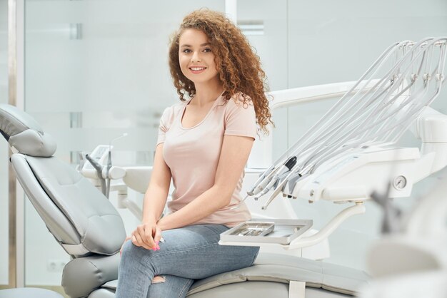 Niña sonriente con el pelo rizado sentada en un sillón dental