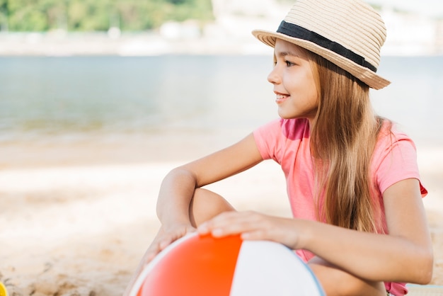 Niña sonriente con pelota inflable en la playa