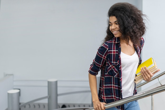 Niña sonriente con pila de libros subir escaleras