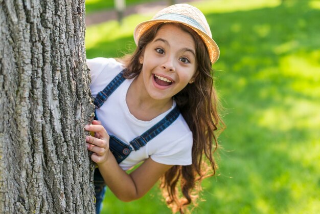 Niña sonriente posando detrás de un árbol