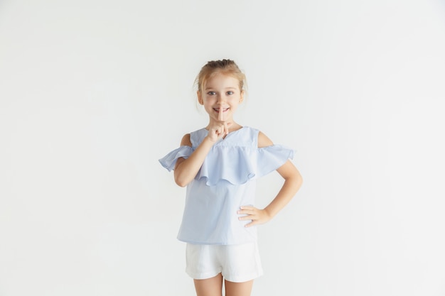 Niña sonriente posando en ropa casual sobre fondo blanco de estudio