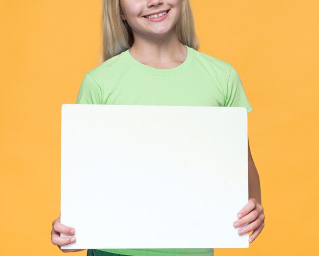 Niña sonriente de primer plano con hoja de papel en blanco