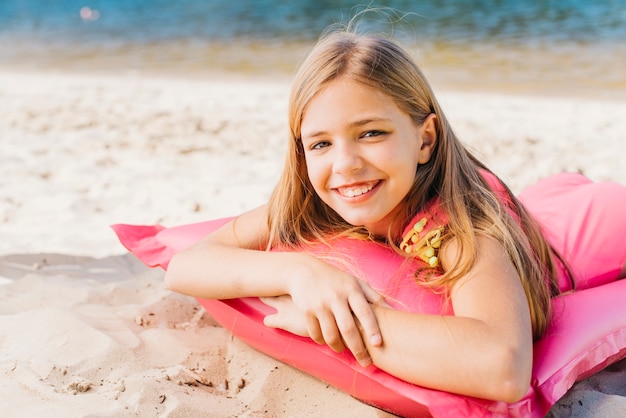 Niña sonriente que se relaja en el colchón de aire en la playa en verano