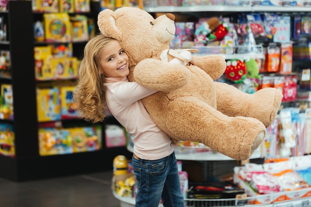 Niña sonriente que sostiene el oso de peluche grande