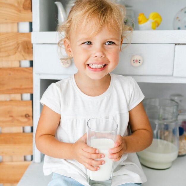 Niña sonriente que sostiene un vaso de leche