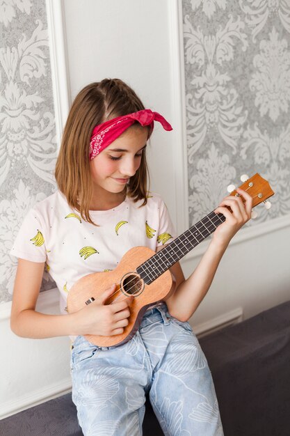 Niña sonriente que toca el ukelele en casa