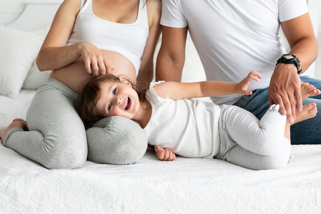 Niña sonriente quedándose en la cama con sus padres