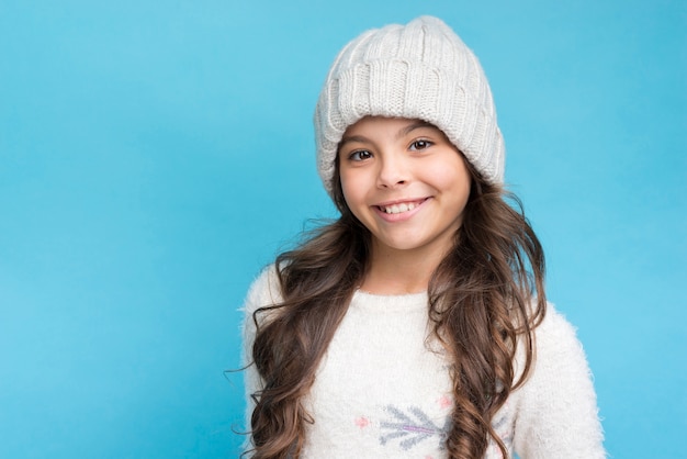 Niña sonriente con sombrero blanco y ropa sobre fondo azul