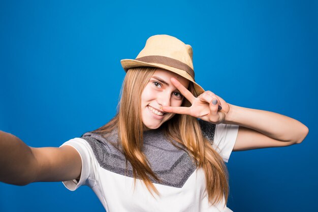 Niña sonriente con sombrero brillante haciendo selfie delante de la pared azul