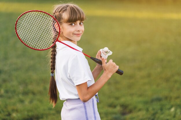 Niña sonriente sosteniendo bádminton sobre su hombro y volante