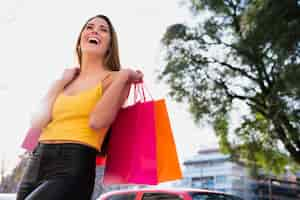 Foto gratuita niña sonriente sosteniendo bolsas con árbol detrás