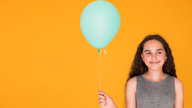 Niña sonriente sosteniendo un globo azul con espacio de copia