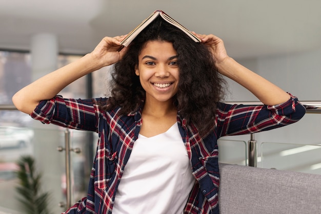 Foto gratuita niña sonriente sosteniendo libro en cabeza