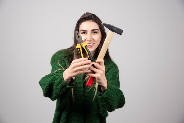 Niña sonriente sosteniendo un martillo y alicates en sus manos.