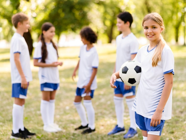 Niña sonriente sosteniendo una pelota de fútbol junto a sus compañeros de equipo