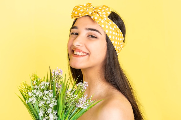 Niña sonriente sosteniendo un ramo de flores y de pie sobre fondo amarillo Foto de alta calidad