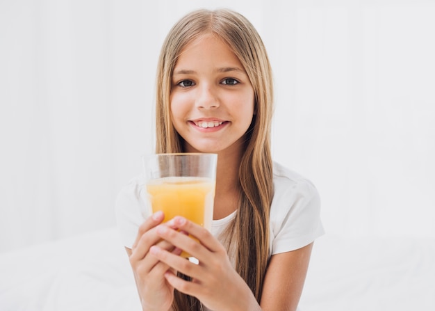 Niña sonriente sosteniendo un vaso de jugo de naranja