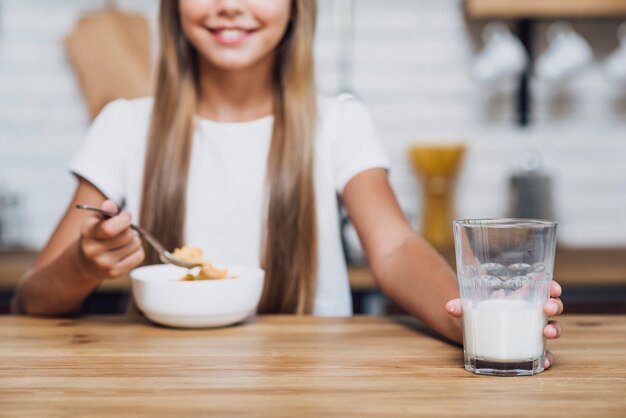 Niña sonriente sosteniendo un vaso de leche mientras come cereal