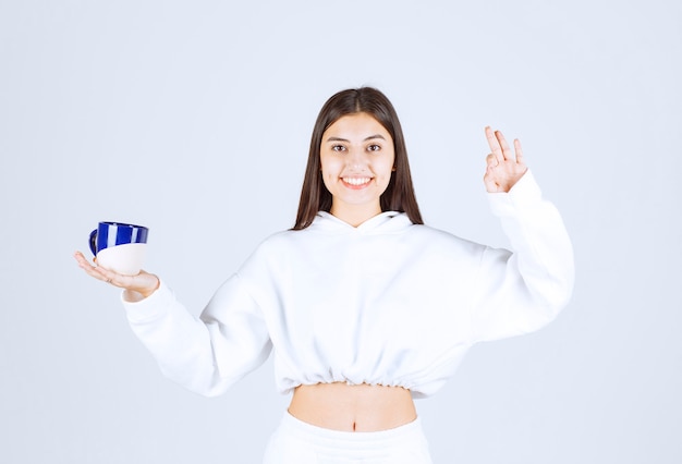 niña sonriente con una taza que muestra gesto bien.