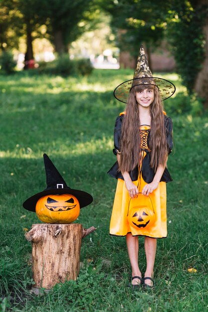 Niña sonriente en traje de bruja cerca de calabaza