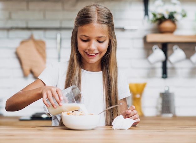 Niña sonriente vertiendo leche en un tazón de cereal