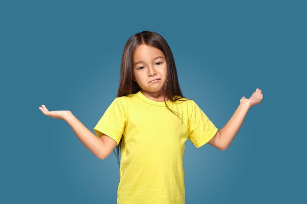 Niña sorprendida con los brazos extendidos sobre fondo azul.