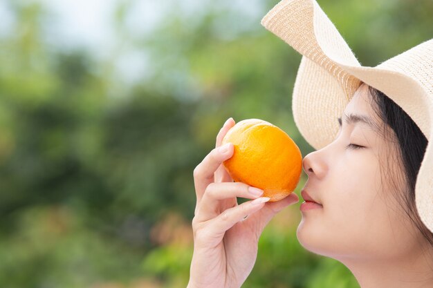 Niña sosteniendo una fruta naranja en su mano y oliéndola