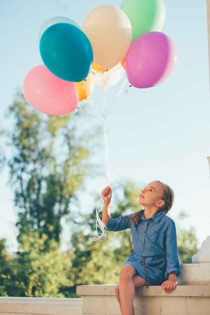 Niña sosteniendo globos de colores mirando hacia ellos