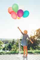 Foto gratuita niña sosteniendo globos de colores que se extiende hacia el cielo y soñando