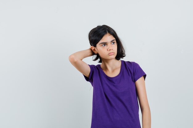 Niña sosteniendo la mano detrás de la cabeza en camiseta y mirando triste.