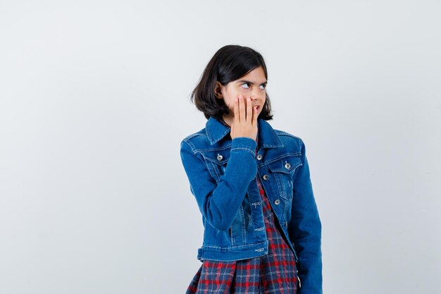 Niña sosteniendo la mano en la mejilla en camisa, chaqueta y mirando pensativo, vista frontal.