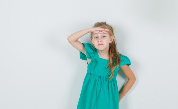 Niña sosteniendo la mano sobre los ojos en vestido verde