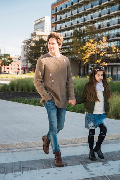 Niña sosteniendo la mano de su padre mientras camina sobre el pavimento