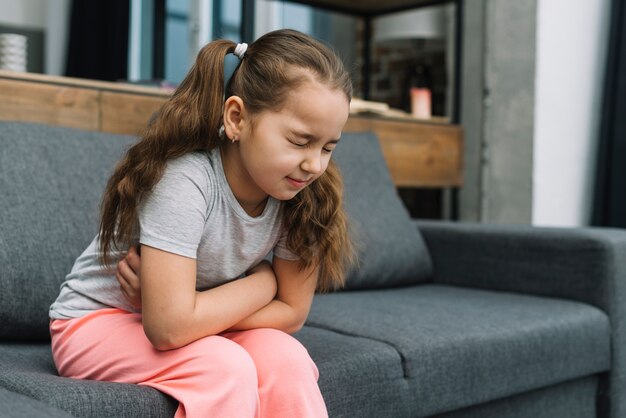 Niña sosteniendo las manos en su estómago sufriendo de dolor