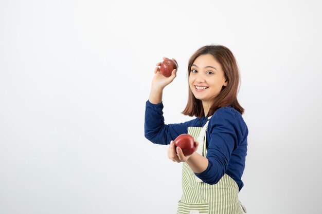 niña sosteniendo manzanas rojas mientras sonríe en blanco.