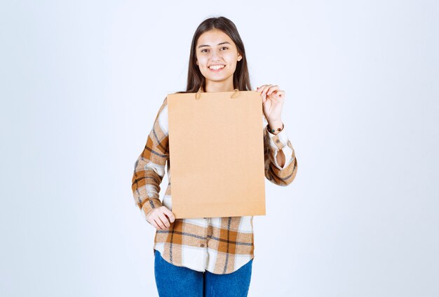 Niña sosteniendo el paquete de artesanía de papel y de pie sobre una pared blanca.