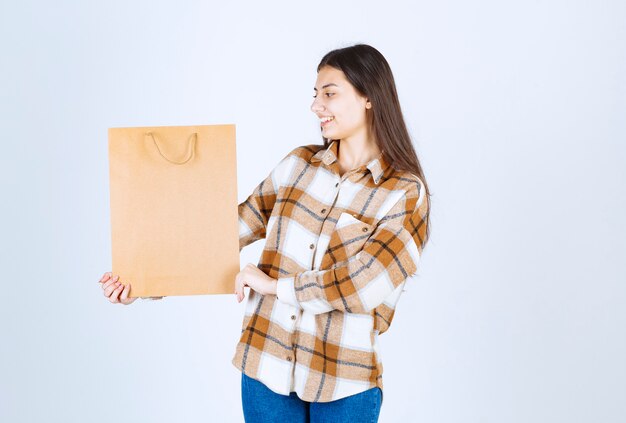 Niña sosteniendo el paquete de artesanía de papel y de pie sobre una pared blanca.