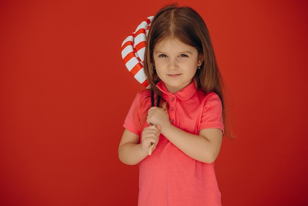 Foto gratuita niña sosteniendo piruleta grande aislado sobre fondo rojo.