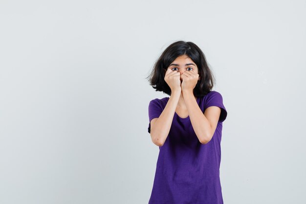 Niña sosteniendo puños en la cara en camiseta y mirando asustado,