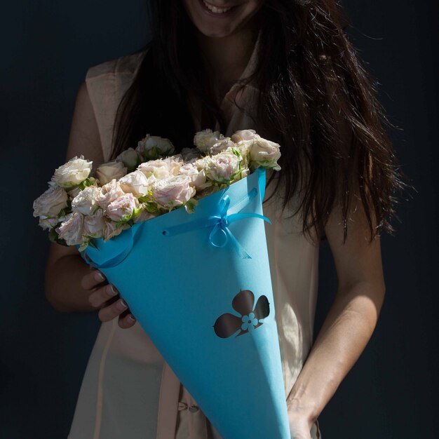 Una niña sosteniendo un ramo de rosas blancas de cartón azul en manos sobre una pared verde