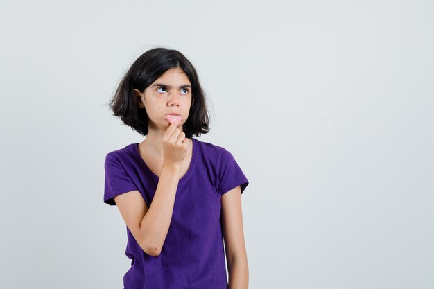 Niña sosteniendo su lengua sacada en camiseta y mirando perpleja.