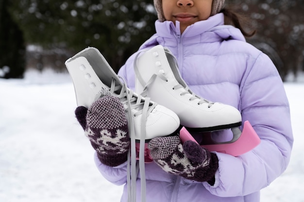 Foto gratuita niña sosteniendo sus patines de hielo en un día de invierno cubierto de nieve