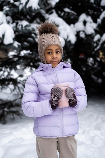 Niña sosteniendo una taza de bebida caliente afuera en un día de invierno