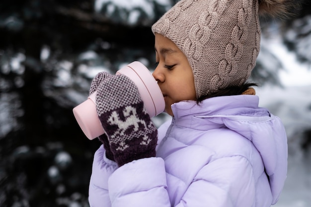 Foto gratuita niña sosteniendo una taza de bebida caliente afuera en un día de invierno