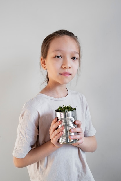 Niña sosteniendo vegetación plantada en maceta reciclada