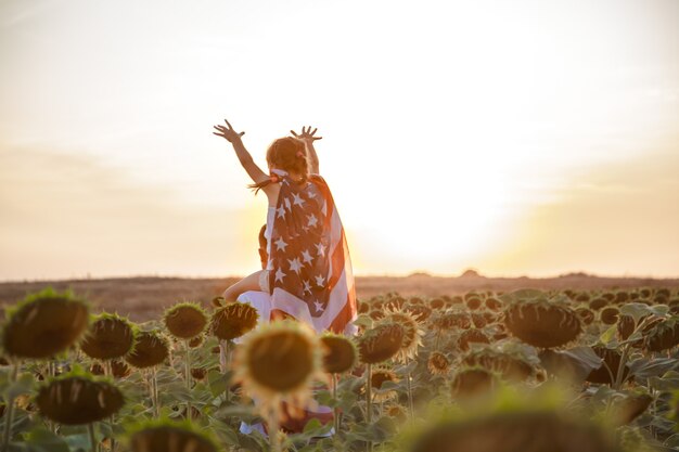 una niña sostiene una bandera estadounidense al atardecer.