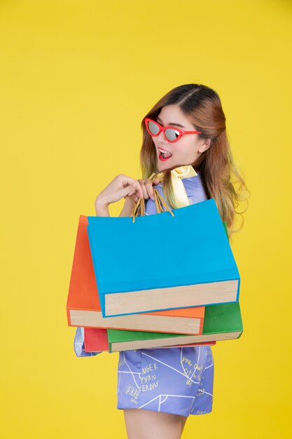 La niña sostiene una bolsa de compras de moda y tiene una tarjeta inteligente sobre un fondo amarillo.