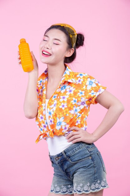 La niña sostiene una botella de jugo de naranja sobre un fondo rosa.