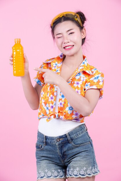 La niña sostiene una botella de jugo de naranja sobre un fondo rosa.