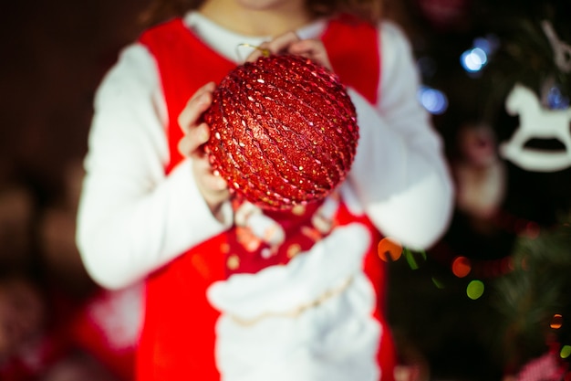 La niña sostiene el juguete rojo del árbol de navidad en sus brazos